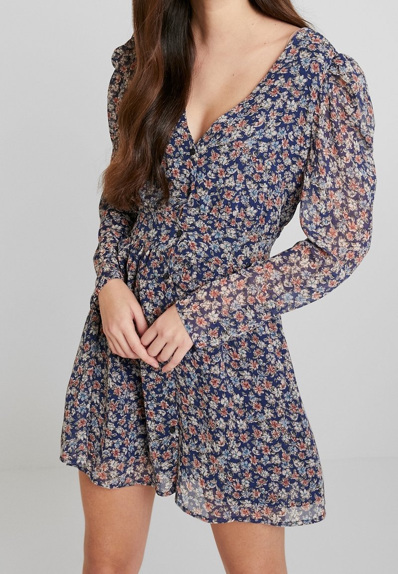 Vestido de estampado floral en navy con escote en V, mangas largas tipo globo, cintura ceñida y una tela ligera y fluida.