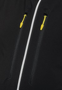 Schwarzer Jackenstoff mit zwei Reißverschlusstaschen. Merkmale sind weiße Reißverschlusszähne und leuchtend gelbe Zuglaschen. Glatte Textur, minimalistisches Design.