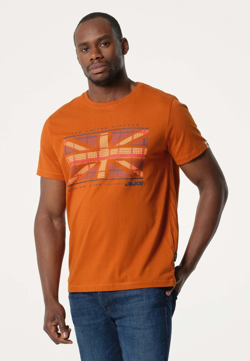 Oranje katoenen T-shirt met korte mouwen en een grafische print van de Britse vlag in rasterpatroon. Gestyleerd met blauwe denim jeans.