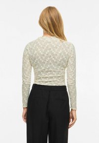 Top in pizzo a maniche lunghe color avorio con motivo floreale, abbinato a pantaloni neri a vita alta. Presenta una texture delicata e una silhouette aderente.