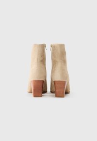 Beige suede ankle boots with a stacked wooden heel, featuring a zipper closure at the back and a smooth texture.