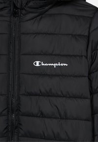 Μαύρο μπουφάν τύπου puffer με οριζόντια καπιτονέ σχεδίαση, μπροστινό φερμουάρ και λευκό λογότυπο Champion στην αριστερή πλευρά του στήθους. Λείος, γυαλιστερός υφής.