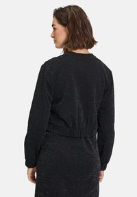Felpa nera con finitura texture e luccicante, colletto rotondo e fascia elastica in vita, dotata di maniche lunghe e vestibilità comoda.