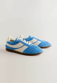 Blauwe suède sneakers met witte leren accenten, voorzien van een zachte binnenvoering, ronde neus en een gestructureerde buitenzool voor grip.