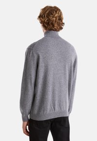 Maglione grigio con colletto alto, polsini a coste e vestibilità comoda. Texture morbida con linee pulite e dettagli minimi, abbinato a pantaloni scuri.