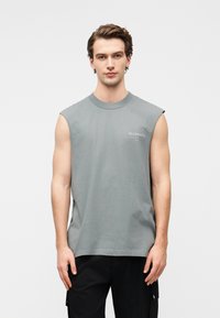 Αμάνικο, ανοιχτό γκρι βαμβακερό t-shirt με στρογγυλή λαιμόκοψη και διακριτική λεπτομέρεια λογότυπου στο στήθος· απαλή υφή και άνετη εφαρμογή.