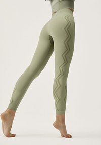 Light green ribbed leggings with a zigzag pattern along the outer side. Smooth, stretchy material, ankle-length design, and seamless waistband.