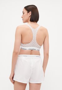 Calvin Klein sportski grudnjak s svijetlosivim uzorkom i crnim logotipom, upotpunjen bijelim šortsevima s odgovarajućom logotipom na struku.