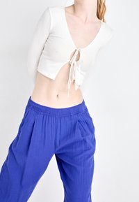 Haut court blanc à manches longues côtelées avec un col en V et un nouage à l'avant, associé à un pantalon bleu ample à taille élastique avec des plis.