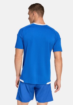 Mężczyzna w niebieskiej koszulce sportowej i szortach, odwrócony tyłem, z białymi lamówkami na rękawach i spodenkach.