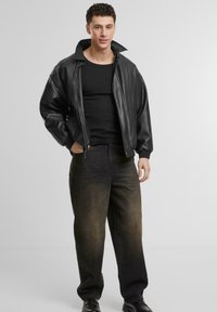 Černá kožená bomber bunda s oversized střihem, nošená přes černý žebrovaný top. V kombinaci s tmavými denimovými džíny s bledým zakončením.