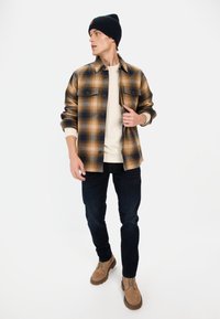 Tjekket flannel skjorte i brun og marineblå, med to brystlommer, lagd over en cremet sweater, parret med mørke jeans og tan støvler.
