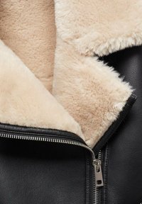 Veste en cuir noir avec doublure en peau de mouton beige et fermeture éclair métallique partiellement ouverte.