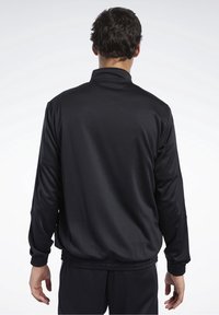 Černá atletická bunda s vysokým límcem, elastickými manžetami a pasem. Vyrobena z hladké látky s volným střihem, navržena pro pohodlí.