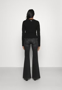 Top de manga larga negro con textura de canalé combinado con pantalones de mezclilla oscuros de pierna acampanada, que presentan un ajuste ceñido en la cintura y una leve campana desde la rodilla hacia abajo.