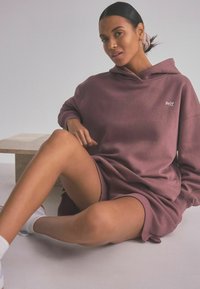 Preveliki maroonski hoodie haljina s kengurskim džepom i bijelim vezom "self.". Glatka tekstura, opušteni kroj i detalji od rebraste obrube.