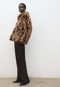 Giacca in pelliccia finta con stampa leopardata, dalla texture morbida, colletto ampio e vestibilità rilassata, abbinata a pantaloni marroni scuri a vita alta e scarpe con punta.