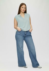 Lichtblauw mouwloos topje met een v-hals en zakdetail, gecombineerd met wijde blauwe jeans. Zilveren puntige schoenen maken de look compleet.