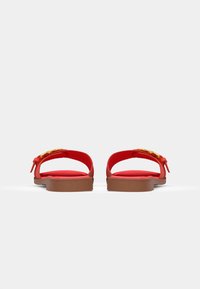 Sandales rouges avec une tige lisse, un dos ouvert et une semelle rembourrée. Comprend un accent doré sur la sangle et une base marron.