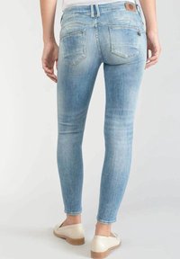 Vaqueros pitillo azul claro hechos de mezclilla con textura desgastada, dos bolsillos traseros y una etiqueta de cuero marrón con la marca en la cintura.