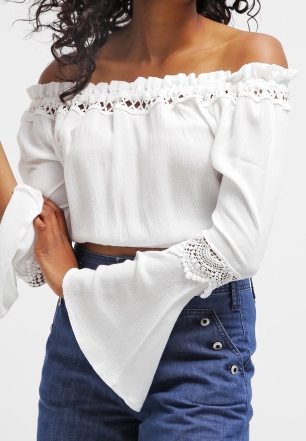 Crop top bianco fuori spalla con scollatura arricciata e maniche a campana, caratterizzato da dettagli in pizzo e un tessuto dalla texture particolare.