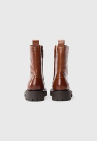 Botas de tobillo de cuero marrón con un acabado suave, suela de goma negra resistente y lengüetas traseras para facilitar el calzado.