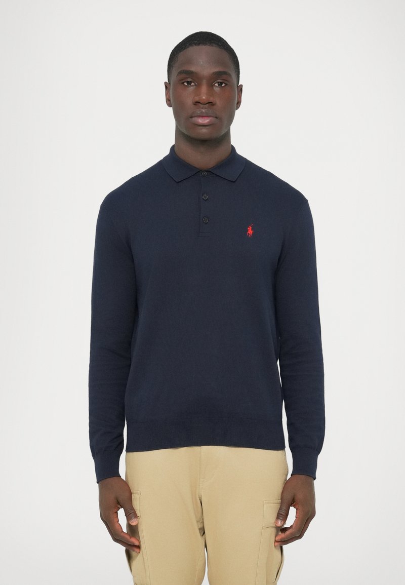 Tengerészkék hosszú ujjú pólópulóver puha kötött anyagból, háromgombos záródással és hímzett piros logóval a bal mellrészen.