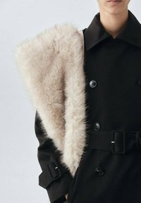 Abrigo negro con un diseño de doble botonadura, que presenta un suave y ligero cuello de piel sintética beige. Incluye botones resistentes y una cintura ceñida con cinturón.