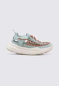 Zapatilla azul clara con detalles de cordones naranjas, que cuenta con una parte superior de malla, una suela blanca acolchada y recortes en los lados para mayor transpirabilidad.