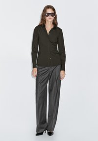 Dark green button-up shirt, tailored fit, long sleeves. Paired with gray wide-leg trousers and black pointed-toe heels.