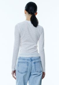 Witte lange mouwen top van getextureerde, geribbelde stof, gecombineerd met lichtblauwe high-waisted denim jeans met achterzakken en een relaxte pasvorm.