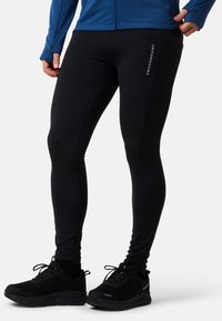 Svarta träningsleggings gjorda av stretchigt material med en avsmalnande design, med en "SWEDEMOUNT"-logotyp på sidan och matchade med svarta sneakers.