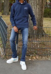 Navyblauwe hoodie met een voorkauwzak en wit logo, gecombineerd met lichtblauwe denim jeans en witte Nike sneakers met blauwe accenten.