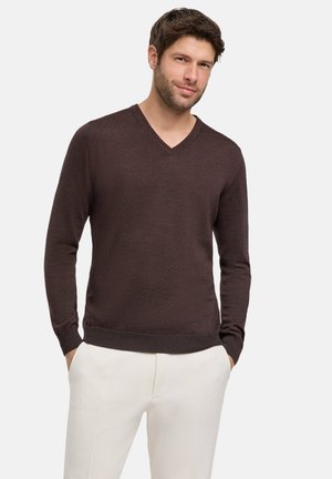Brązowy sweter z dekoltem w serek, wykonany z lekkiego dzianiny o teksturowanym wykończeniu, z prążkowanymi mankietami i dołem, w połączeniu z jasnymi spodniami.