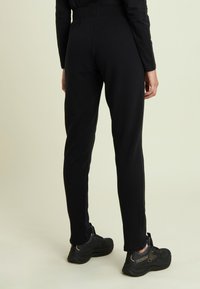 Pantalones deportivos negros con diseño ajustado, hechos con tela suave, con cintura alta y piernas estrechas, combinados con zapatillas negras.