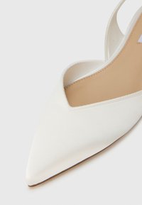 Λευκό σατέν παπούτσι με μυτερή μύτη και λεπτό λουράκι στο πίσω μέρος, με στενό άνοιγμα στη γέφυρα και επίπεδη σόλα.