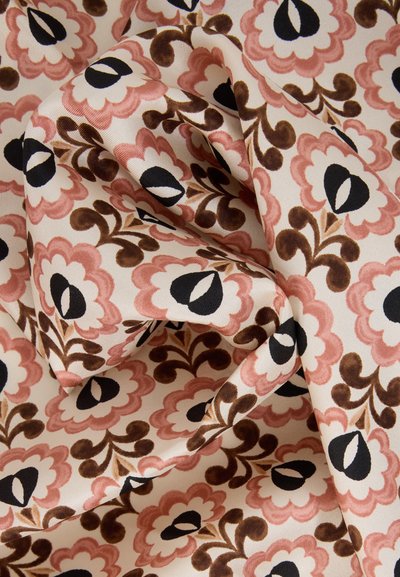 Tissu beige avec des motifs floraux roses et bruns avec des centres noirs et blancs, présenté avec des plis doux et des détails de texture.