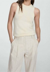Lichtbeige mouwloze gebreide top, gecombineerd met licht gestreepte, hoog gesloten pantalon met voorplooien en zijzakken.