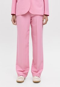 Roze wijde broek gemaakt van een gladde stof, met een getailleerde pasvorm en subtiele plooien aan de voorkant, gecombineerd met lichtgekleurde sneakers.