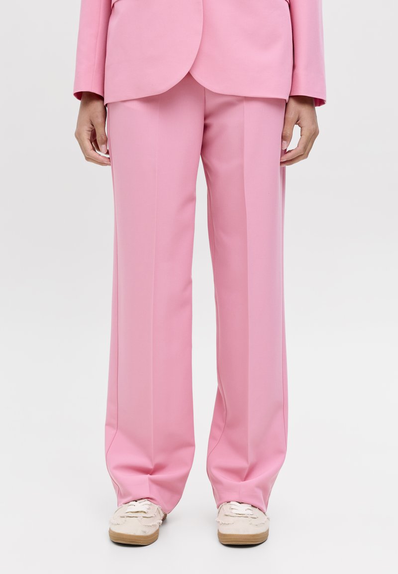 Roze wijde broek gemaakt van een gladde stof, met een getailleerde pasvorm en subtiele plooien aan de voorkant, gecombineerd met lichtgekleurde sneakers.