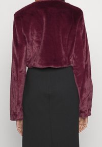 Veste en fausse fourrure bordeaux avec des manches longues et un col arrondi, assortie à une jupe noire ajustée. Texture douce, design court.