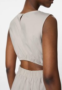 Débardeur beige clair sans manches avec un col rond, détail en trou de serrure au dos et taille élastique, présentant un tissu lisse et un design à côté ouvert.