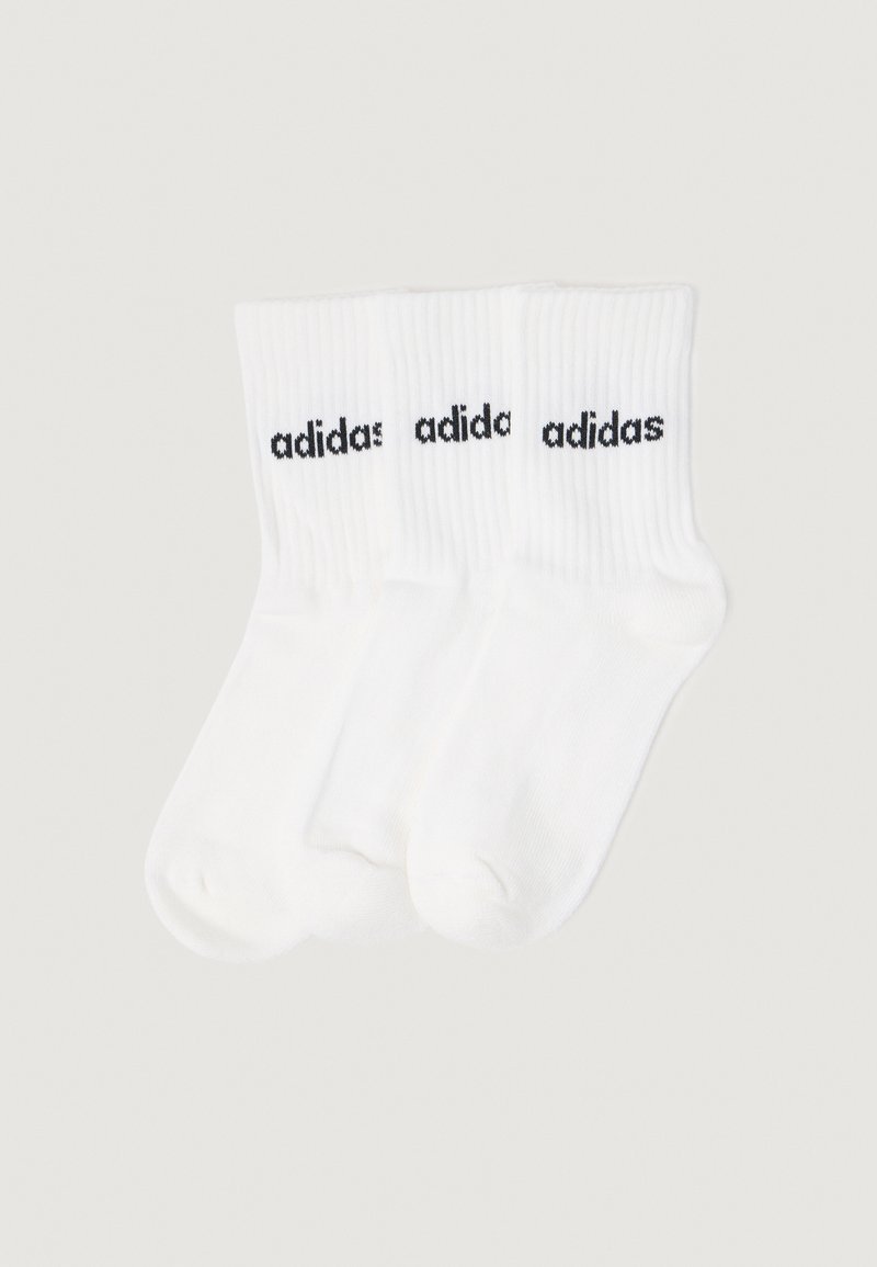 Trzy pary białych skarpetek z prążkowanym wzorem, sięgających do kostek, z czarnymi logo "adidas" na mankietach, wyeksponowane na neutralnym tle.