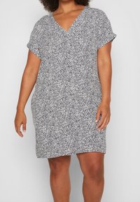 Robe à motifs noir et blanc avec un col en V et des manches courtes, réalisée en tissu léger, avec une coupe décontractée et un ourlet arrivant au genou.