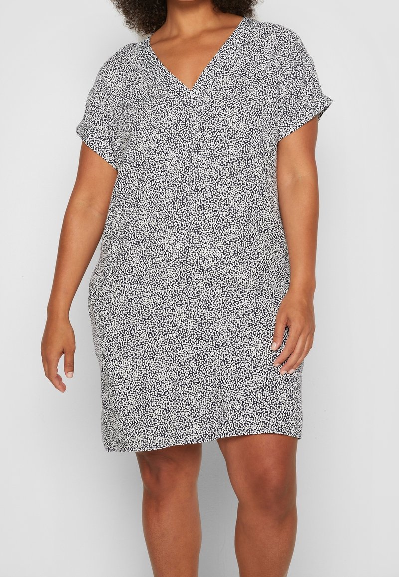 Robe à motifs noir et blanc avec un col en V et des manches courtes, réalisée en tissu léger, avec une coupe décontractée et un ourlet arrivant au genou.