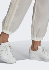 Vitaid ställbyxor med elastiska mudd och beige sidostrad, i kombination med klassiska vita sneakers med texturerad tåkappa och perforeringar.