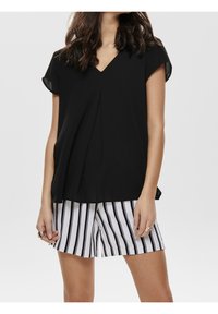 Blusa nera a V con maniche corte, abbinata a pantaloni bianchi con strisce verticali nere. Tessuto morbido e vestibilità comoda.