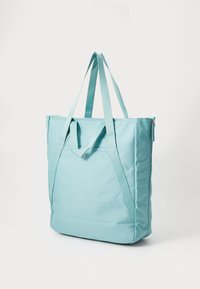 Lichtblauwe totebag met lange en korte handvaten, voorvak met drukknoop en ritsluiting op een witte achtergrond.