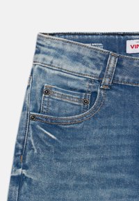 Lys blå denimjeans med en falmet finish. Har en frontlomme med metalnitter, kontrasterende orange søm og et klassisk linning.