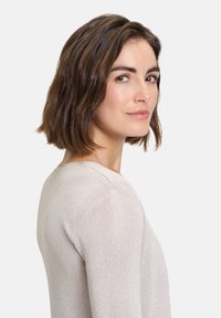 Világos bézs pulóver kerek nyakkal, testhez álló szabással és finom csillogással a textúrában. Simás anyag, bordázott díszítések a mangaszalagokon.